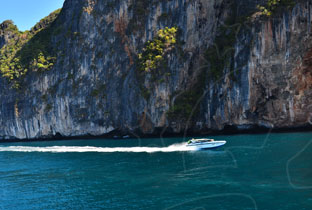 White speedboat cutting through turquoise water beside towering limestone cliffs in Thailand