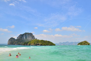 Turquoise sea with limestone karst islands under blue sky, swimmers in shallow water off a tropical beach