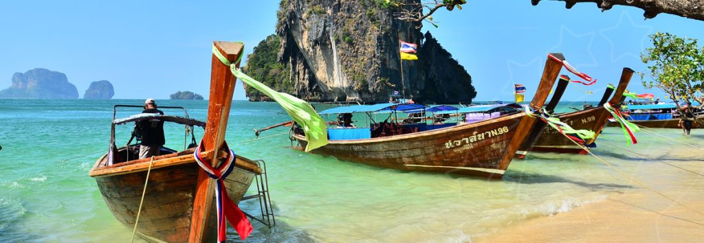 Traditional wooden longtail boats moored in turquoise shallow water near limestone cliffs and sandy beach